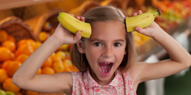 Girl holding bananas as horns in grocery store