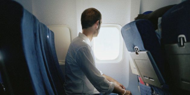 Man sitting in passenger plane, looking through window, side view