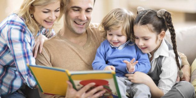 Smiling parents reading a book to their little children.