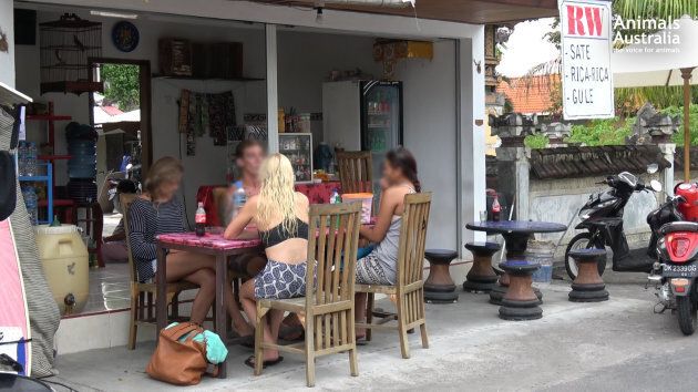 Tourists sit at a Balinese food stall advertising 'RW' for sale. Many tourists don't realise this means dog meat is being sold.