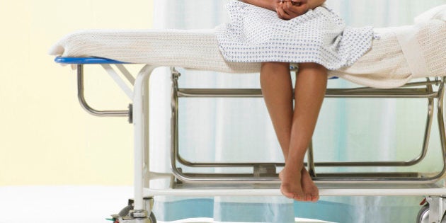 Female patient sitting on gurney in hospital gown, low section