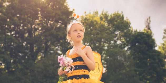A child dressed as a Bumblebee looks up in a stoic pose with a handful of wildflowers.