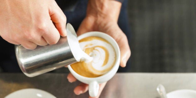 Barista making cappuccino in his coffeeshop or cafe, close-up