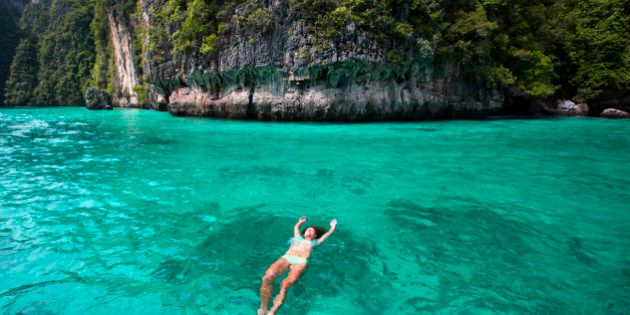 A woman relaxes while floating on her back in the warm turquoise waters of Thailand.