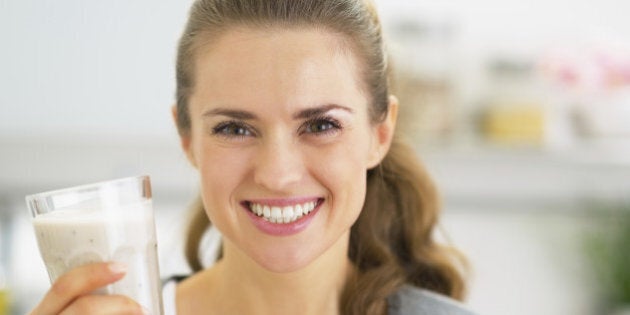 Portrait of happy young woman drinking smoothie in kitchen