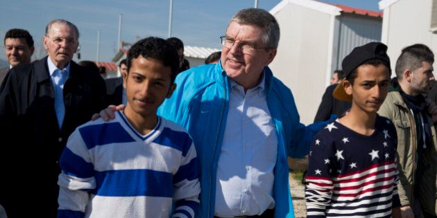 IOC President Thomas Bach, center, walks with two young refugees with former IOC President Jacques Rogge in the background, during their visit at a refugee camp in Athens on Thursday, Jan, 28, 2016. Bach says the torch relay for this year's Olympics in Rio de Janeiro will include a stop at a refugee camp in Athens. He also promised to build sporting facilities on the island of Lesbos that has been hard hit by the migrant crisis.(AP Photo/Petros Giannakouris)
