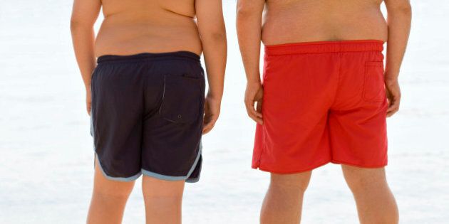 Overweight man and boy standing at beach
