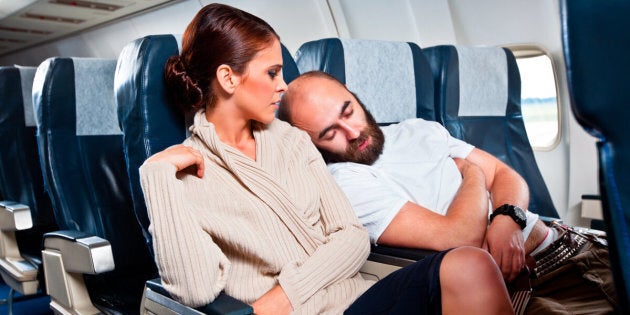 Disgusted woman looking at the sleeping man sitting next to her, who rests his head on her shoulder.