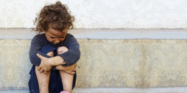 poor, sad little child girl sitting against the concrete wall