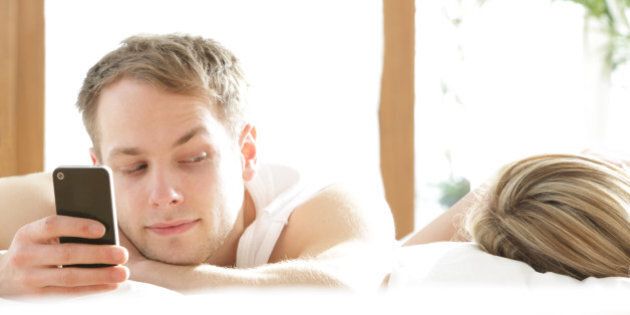 Man with phone in bed, looking at woman asleep