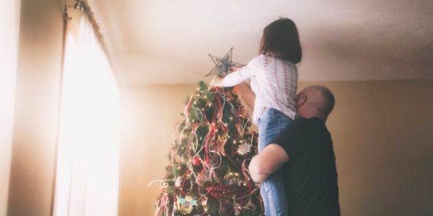 dad lifting daughter to put Star tree topper on Christmas tree