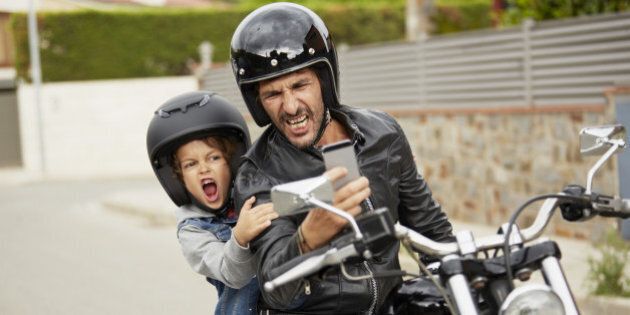 Father and son making faces while taking self portrait through mobile phone on motorbike