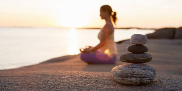 Side view of woman sitting in lotus position on lakeshore with focus on stack of stones
