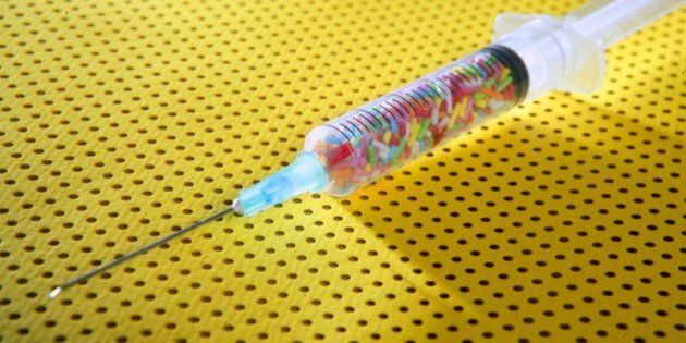 Little colorful candy syringe over yellow background