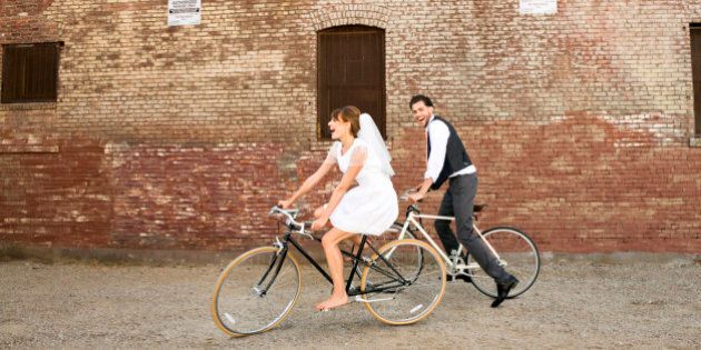 Bride and Groom riding their bikes, horizontal, brick wall