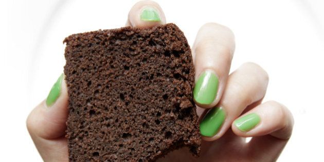 Green nail hand holding bitten chocolate cake.