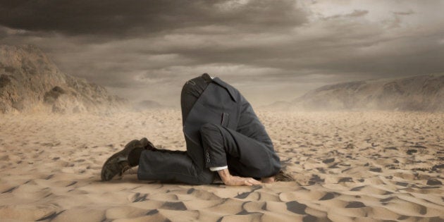 Young businessman hiding head in the sand