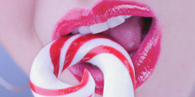 Young woman eating candycane, close-up of mouth