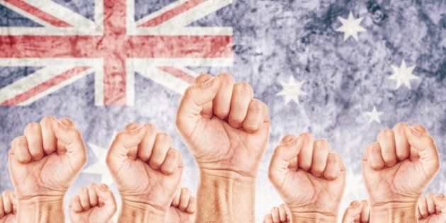 Australia Labor movement, workers union strike concept with male fists raised in the air fighting for their rights, Australian national flag in out of focus background.