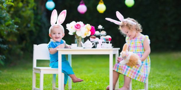 Little boy and girl play toy tea party outdoors. Children with bunny ears on Easter egg hunt. Kids playing in the garden in spring. Toddler and baby with toy rabbit and doll dishes. Family celebration