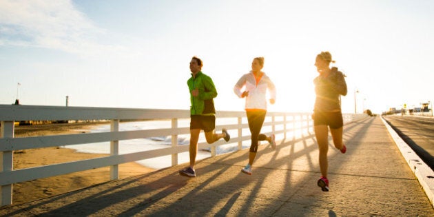 Friends running a boardwalk near the Pacific Ocean.