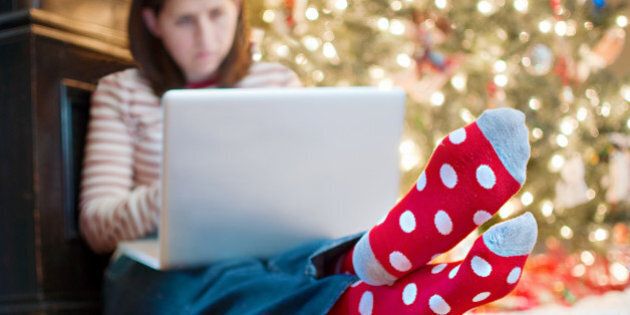 Young woman typing on laptop in front of Christmas tree.