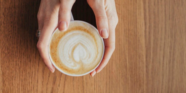 Hands holding cup of coffee with leaf drawn in milk