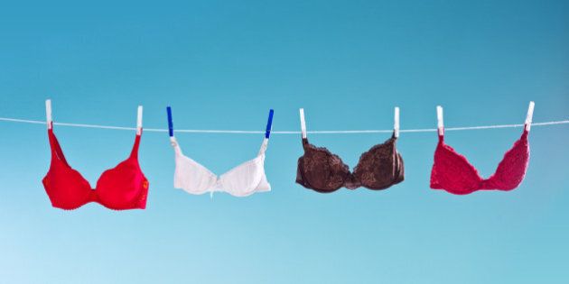 Laundry hangs out on a clothesline to dry. Colorful bras hanging against blue background. Summer time.