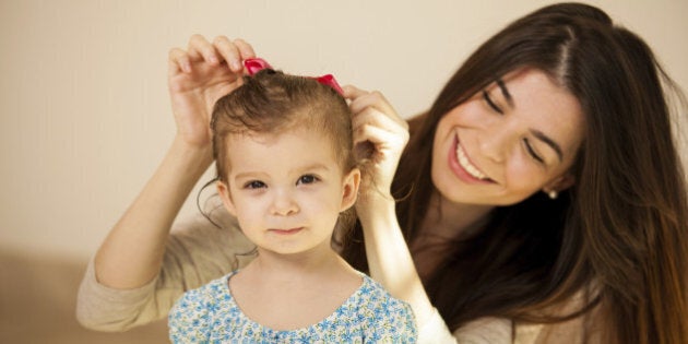 Pretty little Hispanic girl getting her hair done by her mom before they go out together