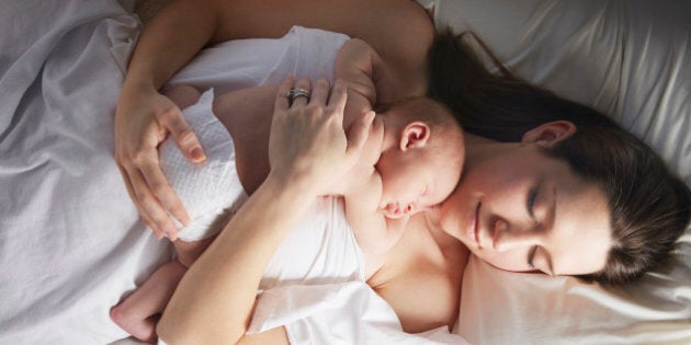 Mother sleeping with newborn baby on bed