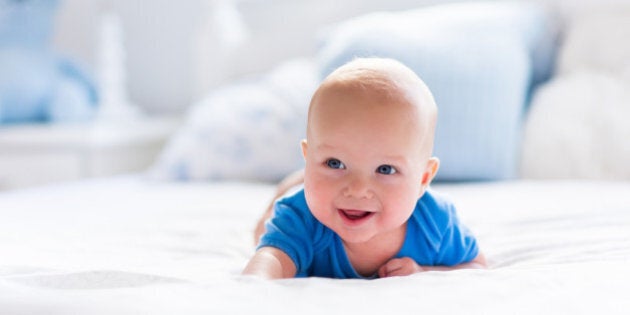 Adorable baby boy in white sunny bedroom. Newborn child relaxing in bed. Nursery for young children. Textile and bedding for kids. Family morning at home. New born kid during tummy time with toy bear.