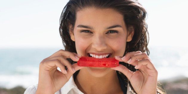 Beautiful woman eating a slice of watermelon on the beach