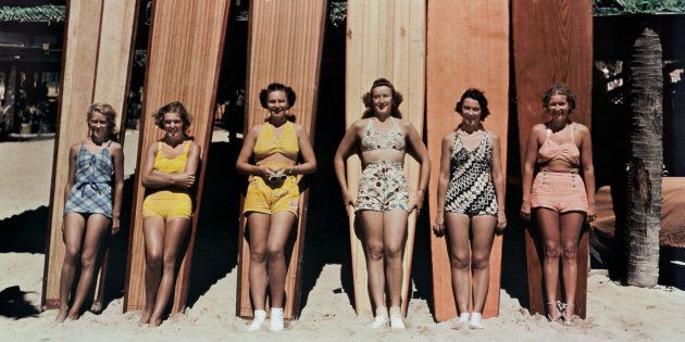 Women pose in front of surfboards on Waikiki Beach in Honolulu, Hawaii, in a photo from a 1938 issue of National Geographic. Their bare beach legs are very contemporary—a couple of decades prior, they might have been wearing stockings.