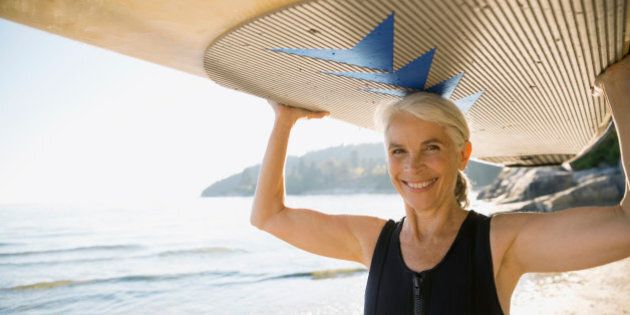 Senior woman holding paddle board overhead on beach