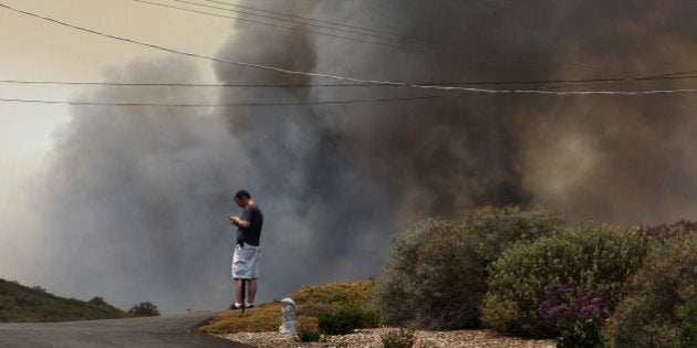 SAN MARCOS, CA - MAY 15: A resident looks at his phone as smoke from the southeast flank of the Cocos fire bears down on houses near Del Dios Highway on May 15, 2014 near San Marcos, California. Fire agencies throughout the state are scrambling to prepare for what is expected to be a dangerous year of wildfires in this third year of extreme drought in California. (Photo by David McNew/Getty Images)