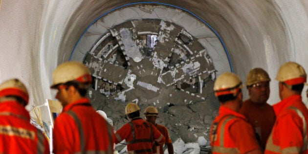 Crossrail workers stand, backdropped by a thousand tonne tunnelling machine, after it breaks through some 35 meters underground at Whitechapel, in east London, Friday, April 4, 2014. The breakthrough will create over a kilometer of new platform and passenger tunnels for the new Crossrail station, and it marks the completion of some 19 miles of tunnels, out of the 26 total, needed to complete the construction of Crossrailâs train tunnels. The tunneling machine with a 7.1m diameter cutterhead is being used for the massive Crossrail project which will link many parts of the London transport network to cut journey times and alleviate congestion, with a scheduled completion in five years. (AP Photo/Lefteris Pitarakis)