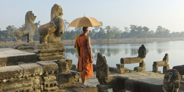 Cambodia, Siem Reap, Angkor Wat, Sras Srang, Buddhist monk standing next to stone carvings and lake.