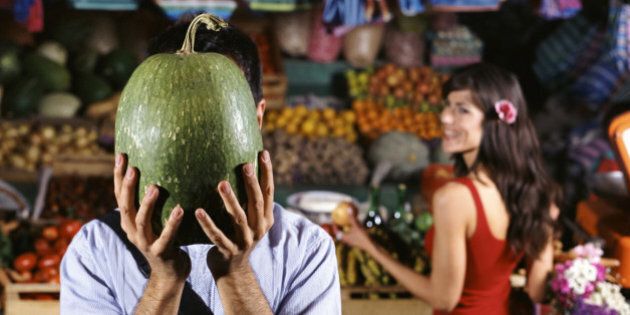 Man Stands by a Market Stall Holding a Watermelon in Front of His Face