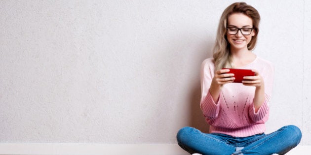 Happy beautiful woman sitting on the floor and using smartphone