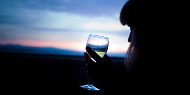 A woman drinks a glass of wine and watches the sunset over Lake Taupo, New Zealand.