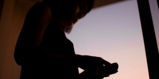 Playing with her smartphone at the window during sunset.