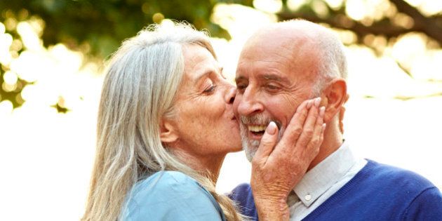 Loving senior woman kissing man on cheek during social gathering in yard