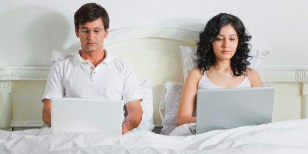 Young couple using laptops in bed