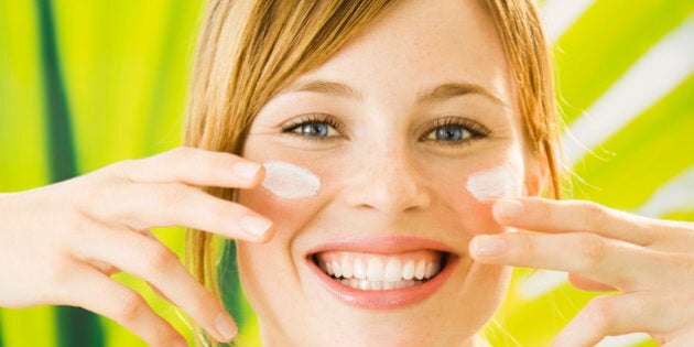 Young woman putting cream on face, smiling, portrait