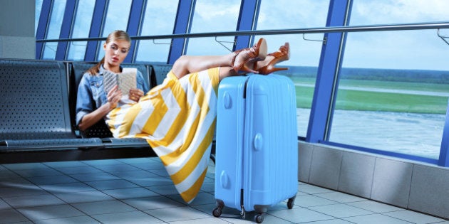 Young adult woman waiting for her flight at the airport lounge and watching boarding pass.