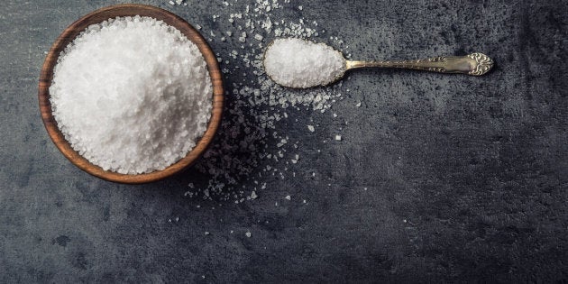 Salt. Coarse grained sea salt on granite - concrete stone background with vintage spoon and wooden bowl.