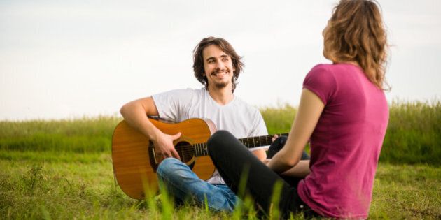 Young man playing guitar to his girlfriend in nature - dating couple