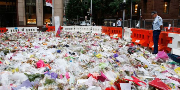SYDNEY, AUSTRALIA - DECEMBER 23: (AUSTRALIA & NEW ZEALAND OUT) A Police officer watches flowers before being removed from the Memorial of the victims of the siege in Martin Place on December 23, 2014 in Sydney, Australia. Volunteers have gathered at Martin Place this morning to begin clearing the thousands of bouquets and cards left in tribute to Tori Johnnson and Katrina Dawson, who were killed in last week's hostage siege at the Lindt Cafe. (Photo by Daniel Munoz/Fairfax Media via Getty Images)
