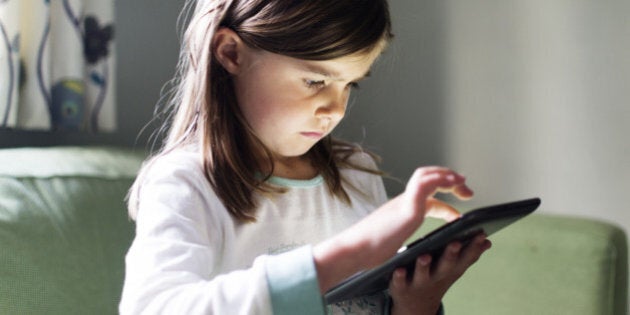 A young girl uses a tablet computer late at night with the glow from the screen on her face.