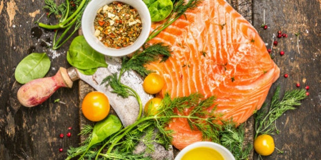 fresh salmon fillet with fresh healthy herbs,vegetables, oil and spices on rustic wooden background, top view